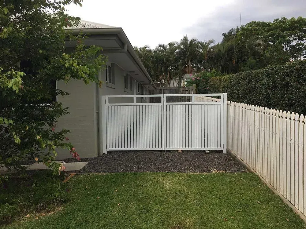 A white fence surrounds a lush green yard in front of a house. — Sunshine Gates in Kunda Park, QLD
