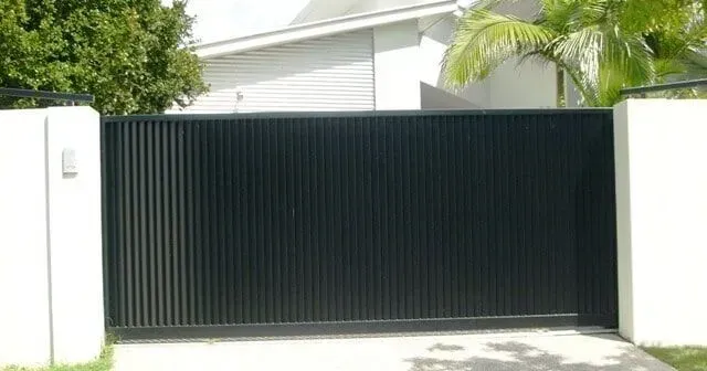 A black sliding gate is open to a driveway in front of a house. — Sunshine Gates in Kunda Park, QLD