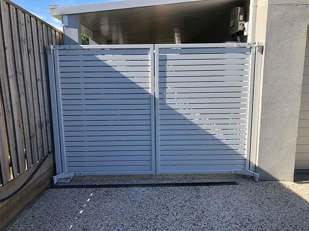 A white gate is sitting next to a wooden fence. — Sunshine Gates in Kunda Park, QLD