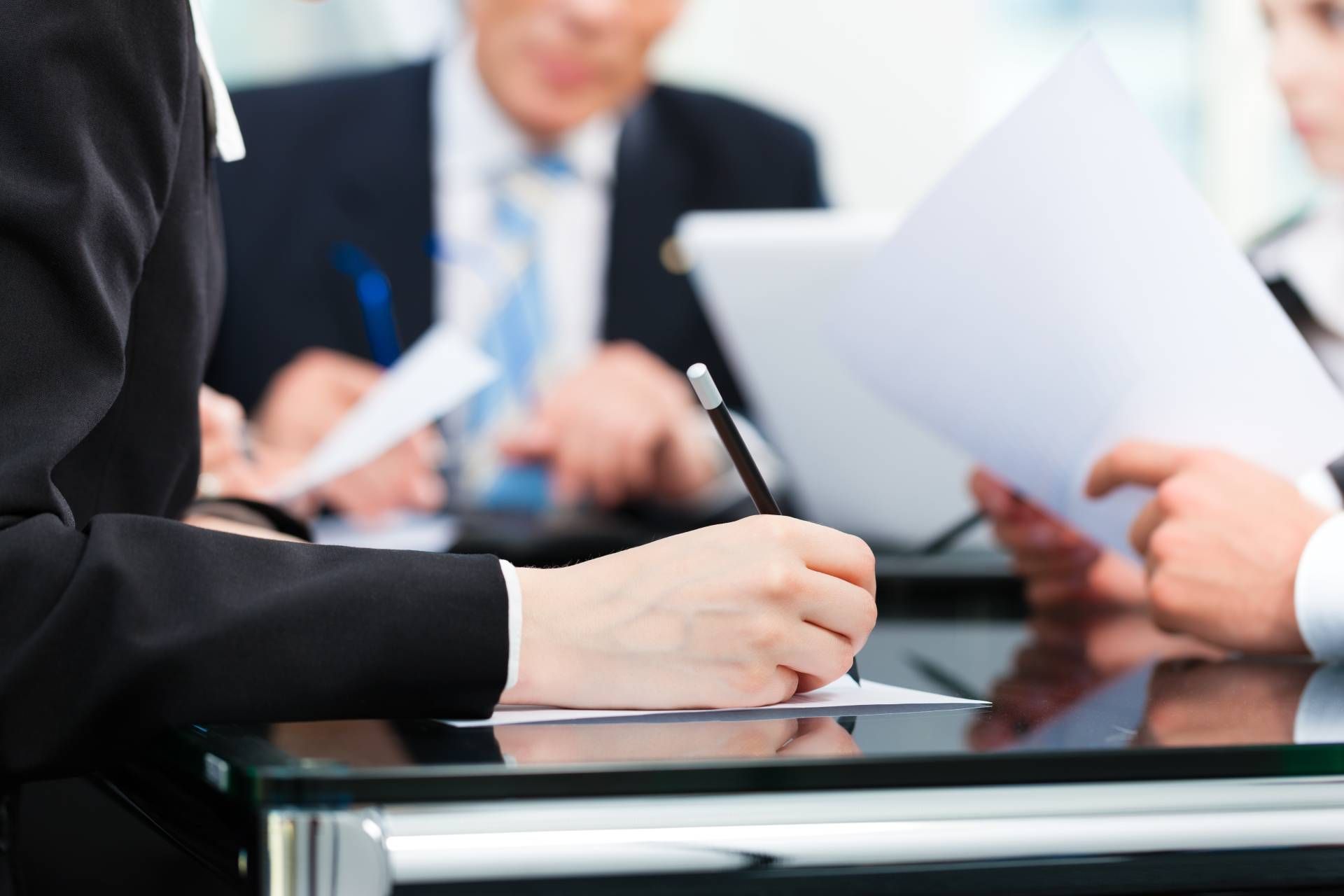 Businesspeople at a table reviewing documents, one person writing with a pen.