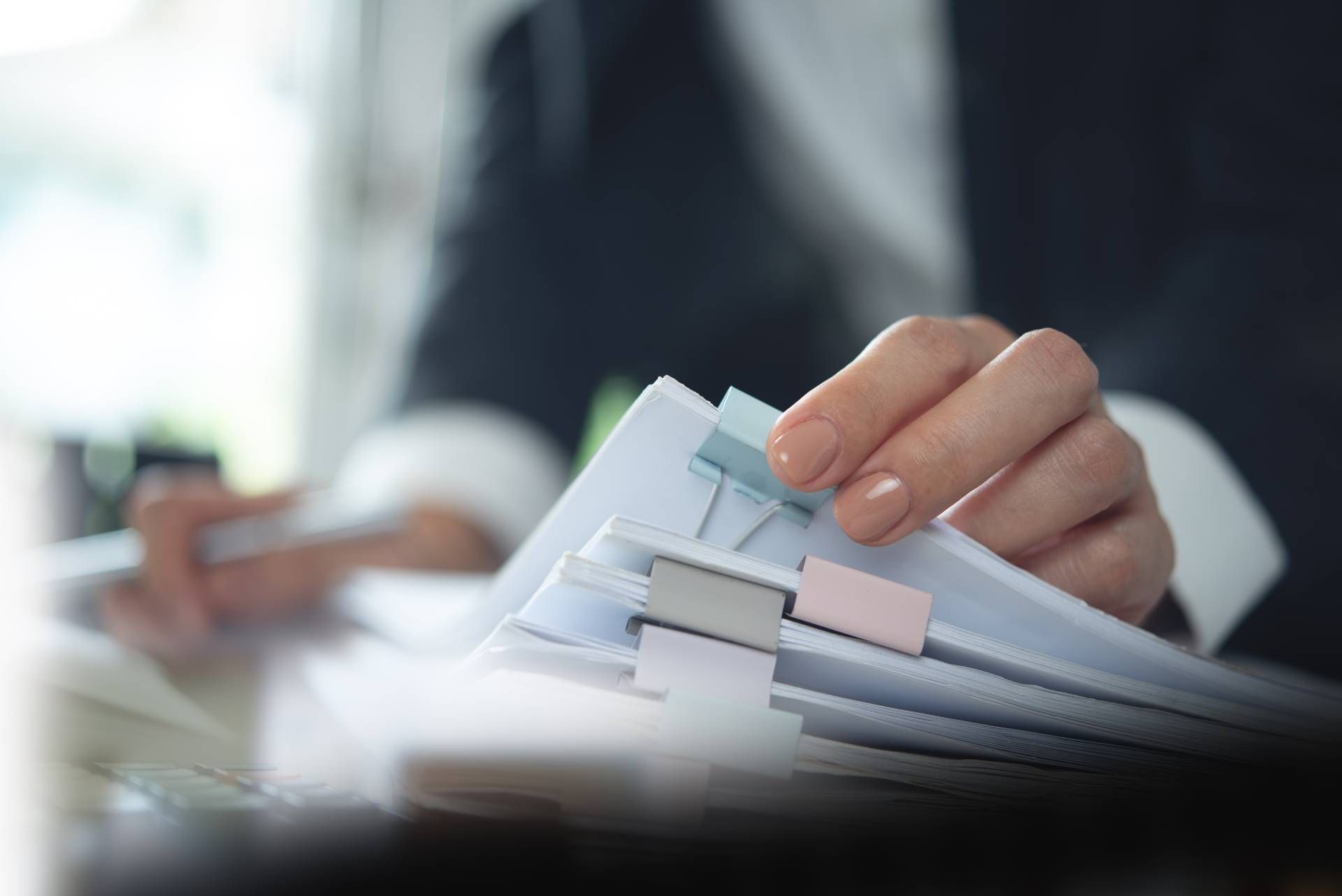 Person in suit holding a stack of papers with colorful tabs, possibly organizing or reviewing documents.