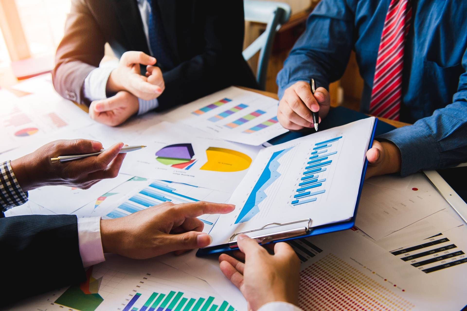 Three people in suits reviewing charts and graphs at a table.