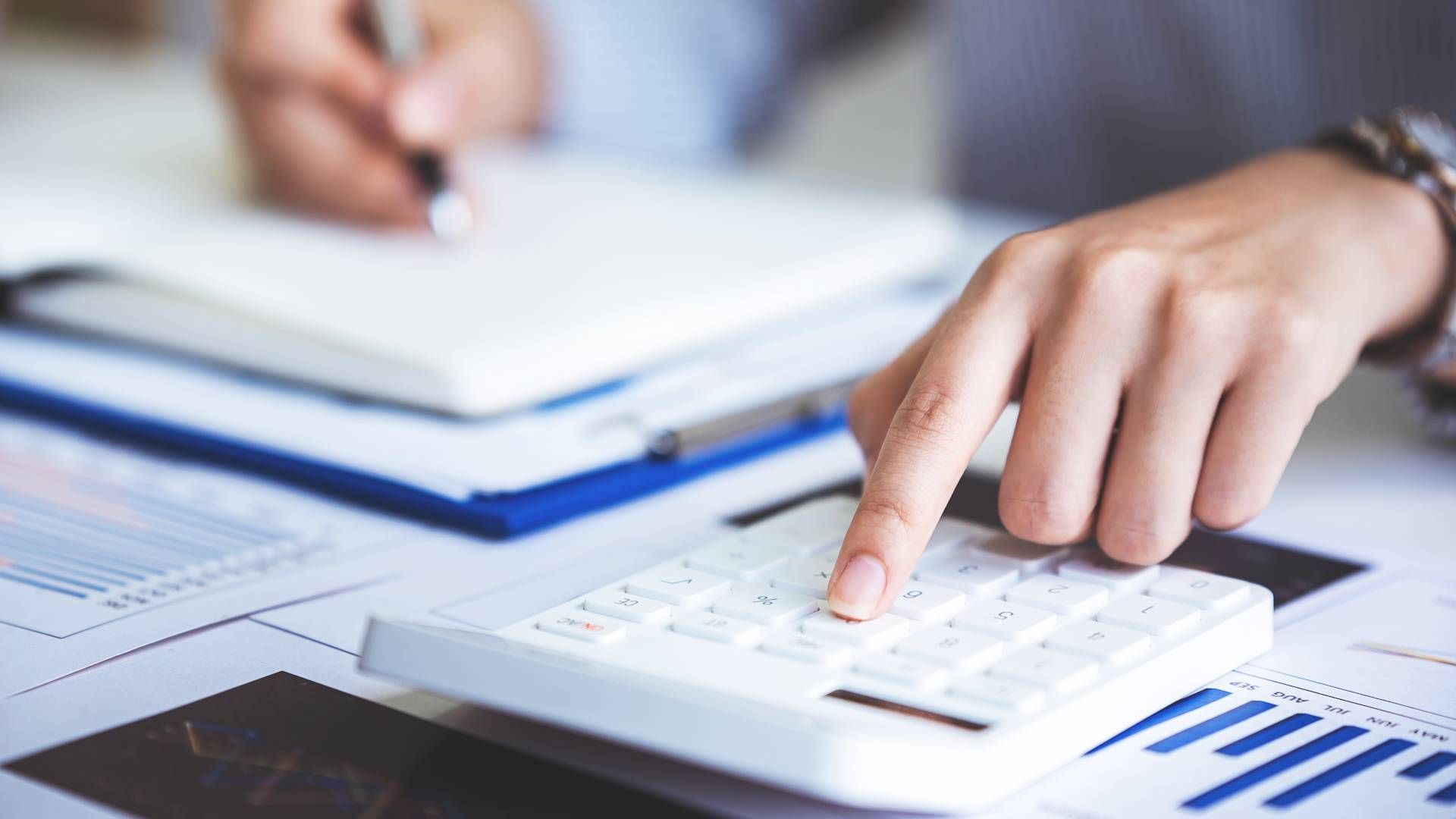 Person using a calculator and writing in a notebook, with financial documents visible.