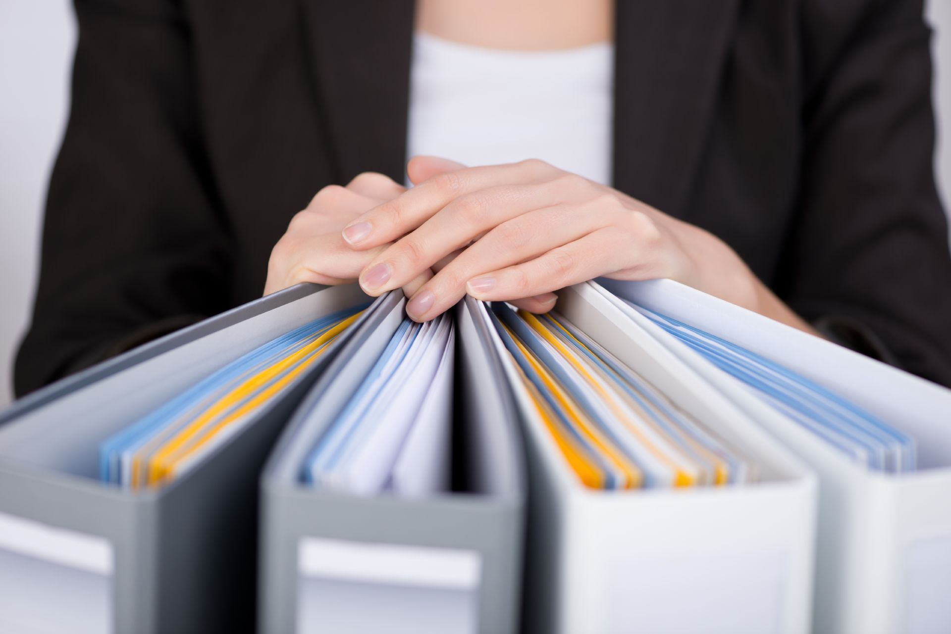 Person's hands resting on top of several organized binders.