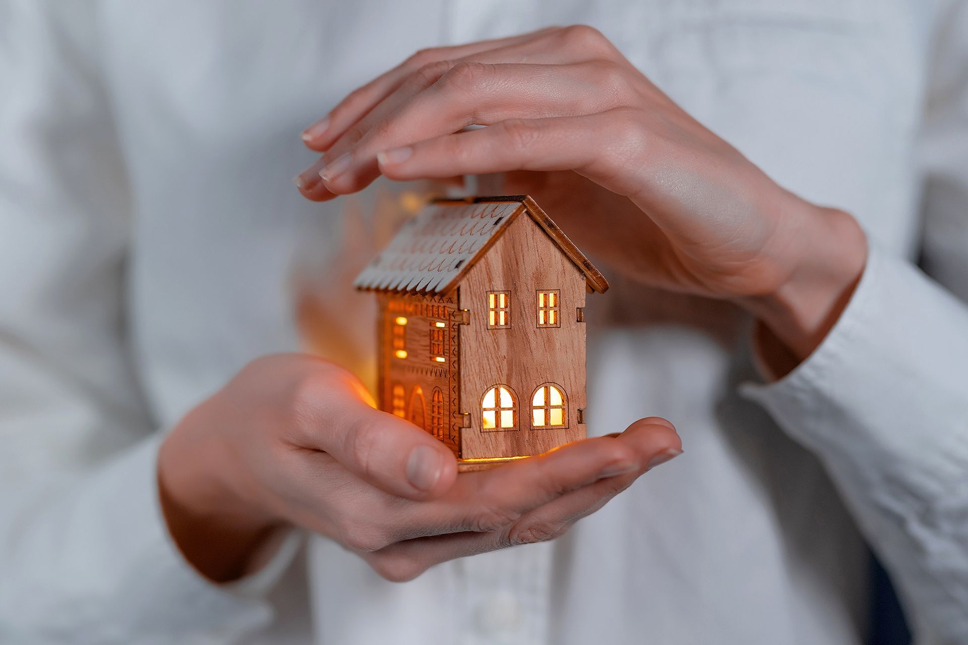 A person is holding a small wooden house in their hands.