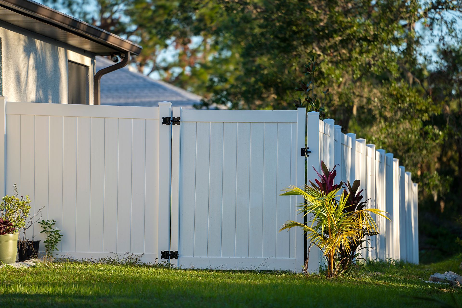 A white fence surrounds a lush green yard in front of a house.