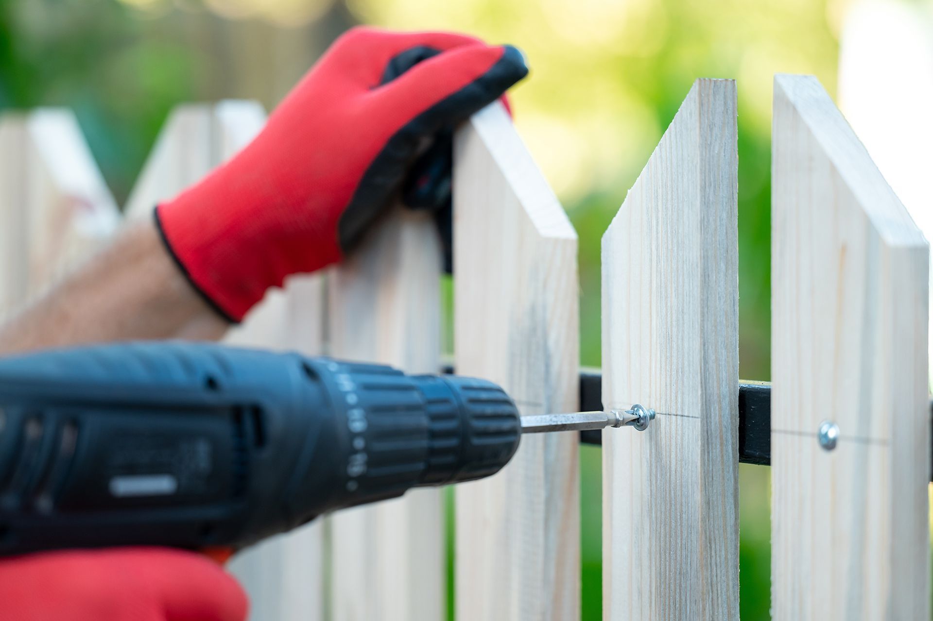 A man is installing a wooden fence with a drill.