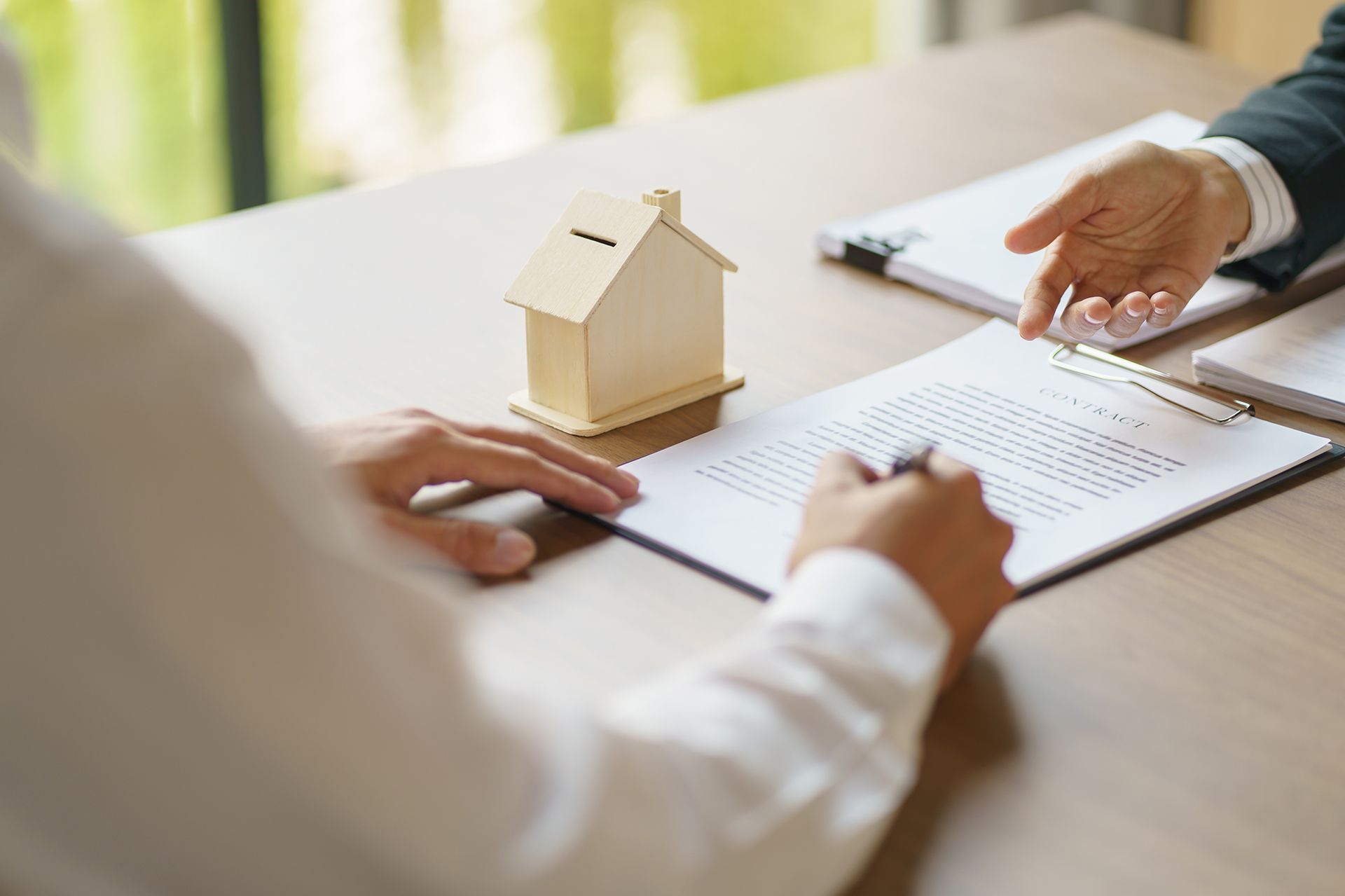 A person is sitting at a table with a model house and a clipboard.