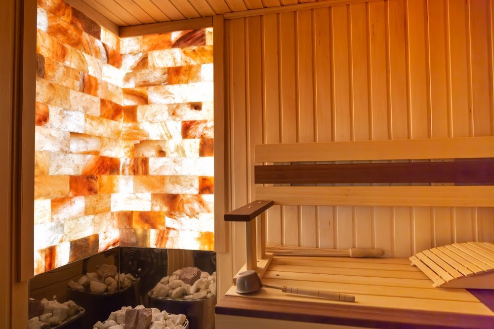 Interior view of a sauna with wooden benches and a wall of illuminated salt bricks.