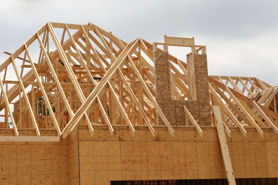 Wooden house frame construction; rafters and sheathing boards visible against a cloudy sky.