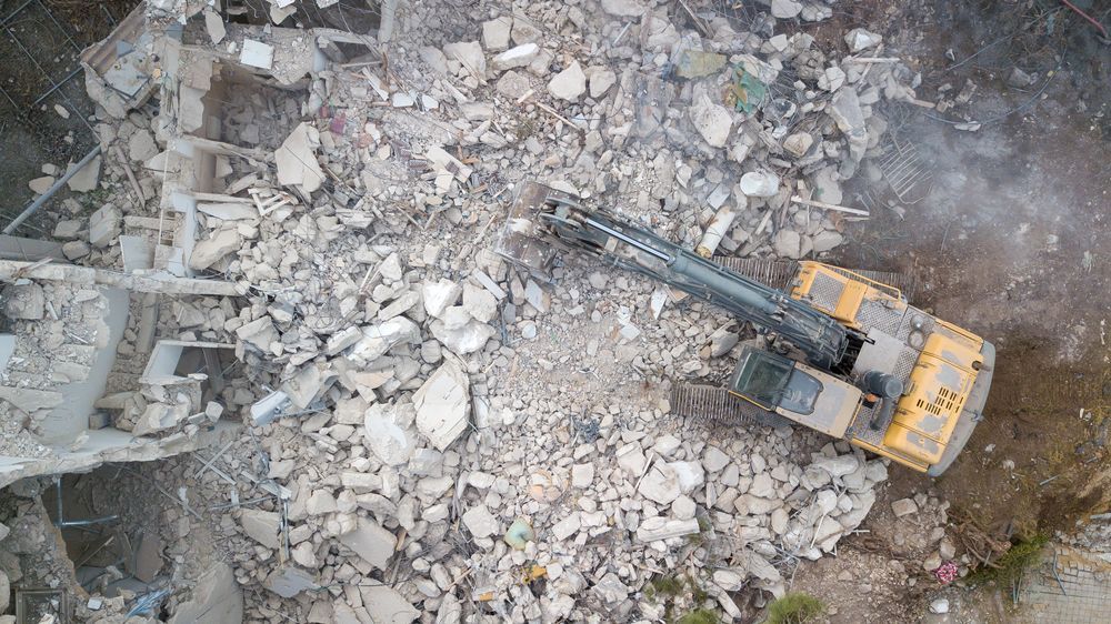 Overhead view of a yellow excavator demolishing a building, surrounded by rubble.