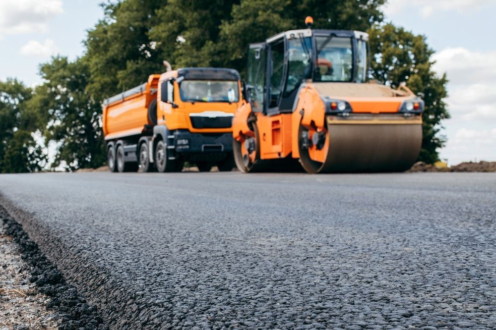 Orange dump truck and road roller on freshly paved asphalt road.