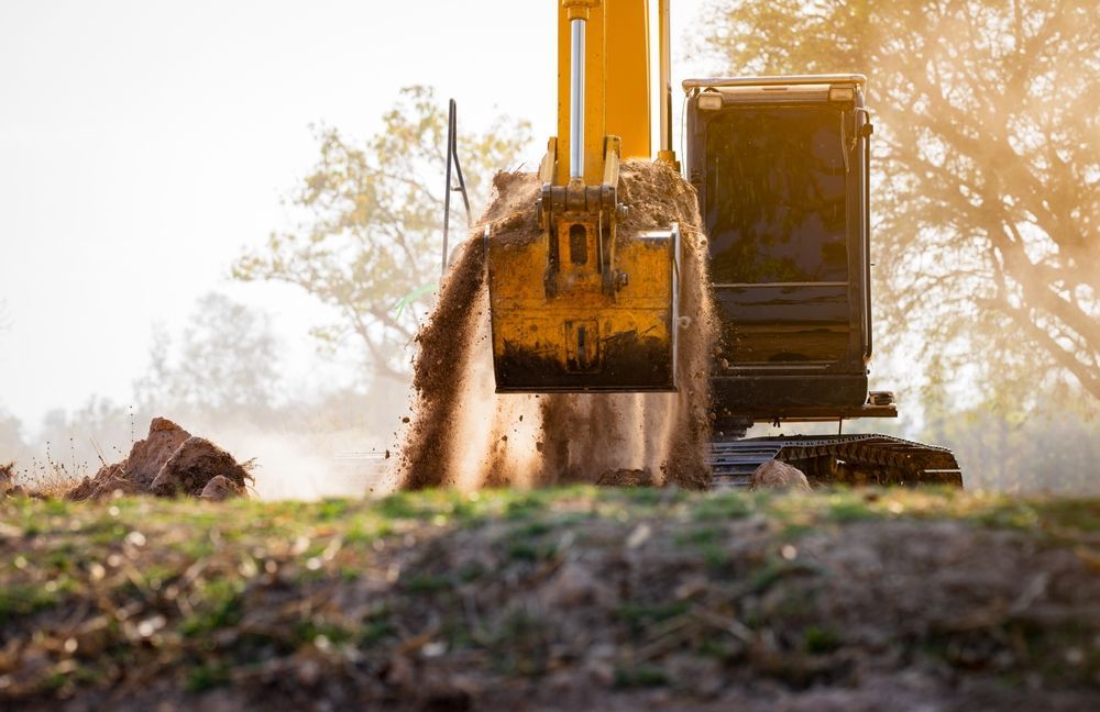 Yellow excavator digging earth, backlit by sunlight.