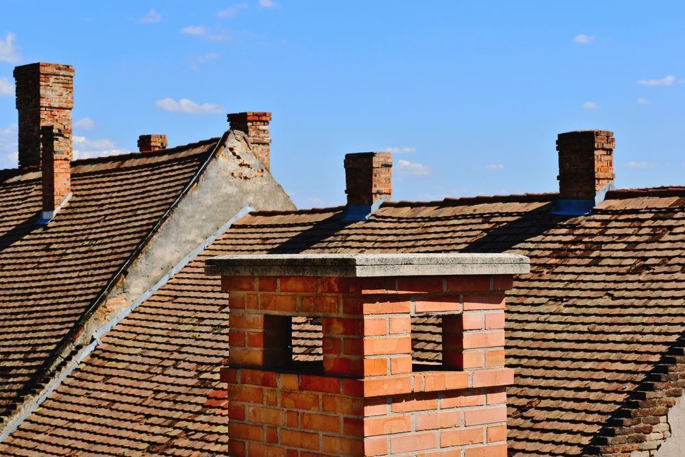 Brick chimneys on brown tiled roofs against a blue sky.