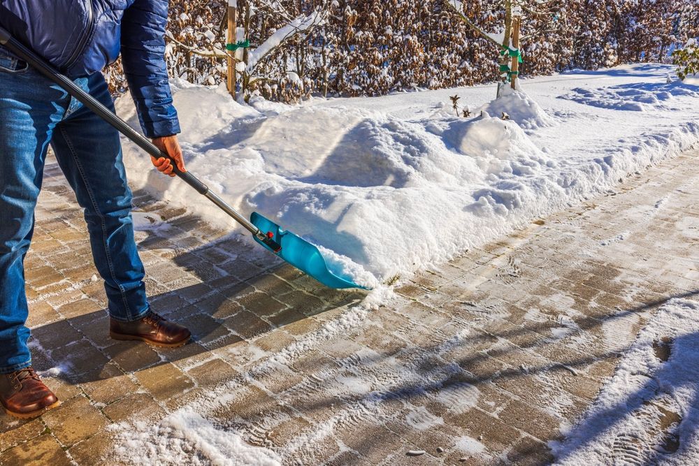 Person shoveling snow from a brick pathway on a sunny winter day.