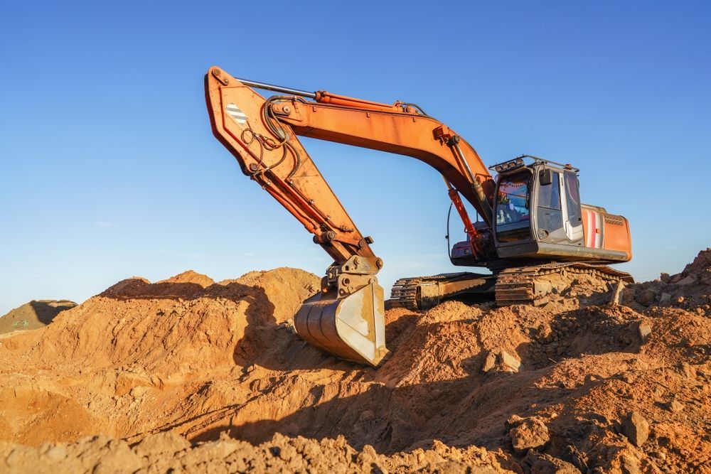 Orange excavator on a pile of dirt, blue sky background.