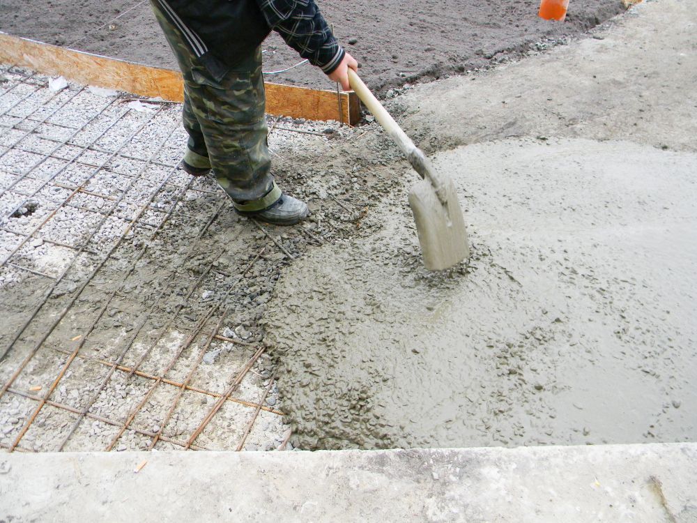 Person shoveling concrete over a metal mesh, preparing a surface.