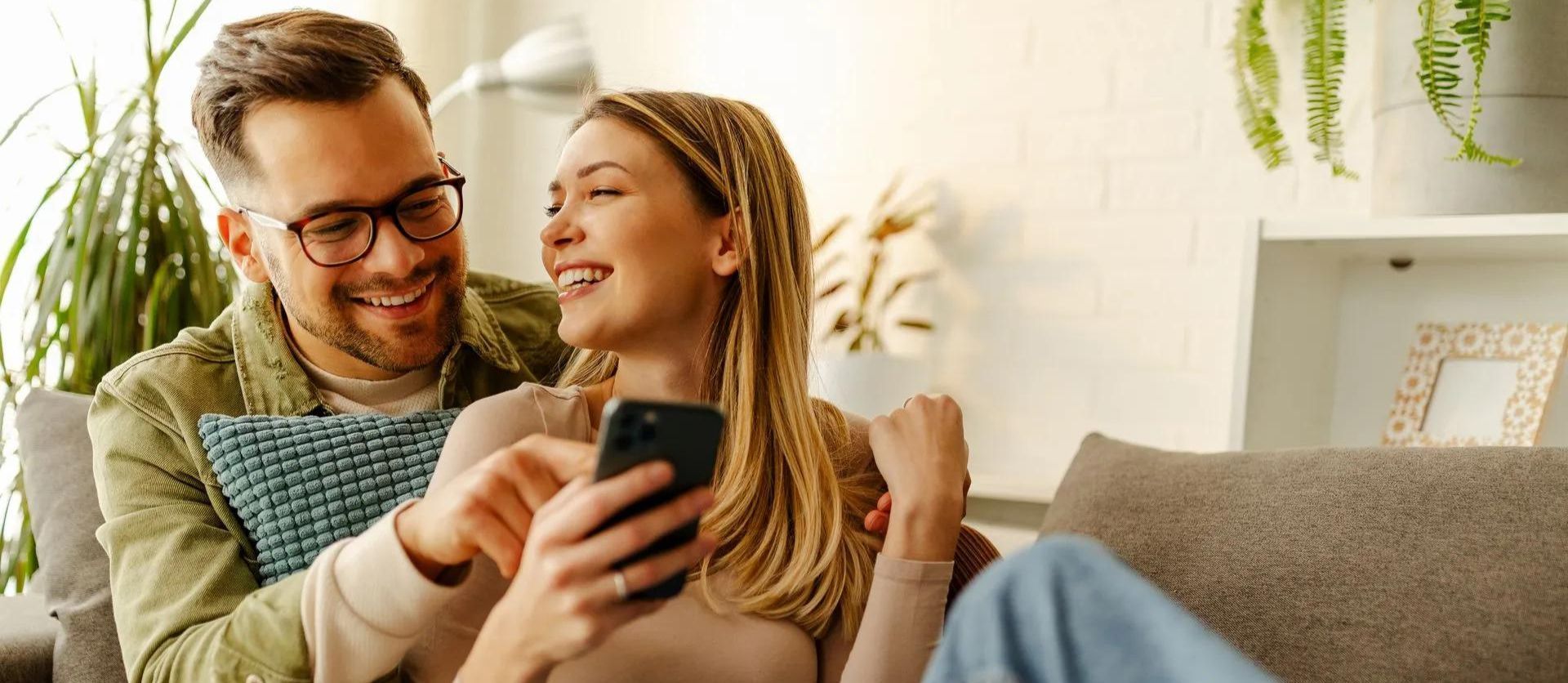 A man and a woman are sitting on a couch looking at a cell phone.
