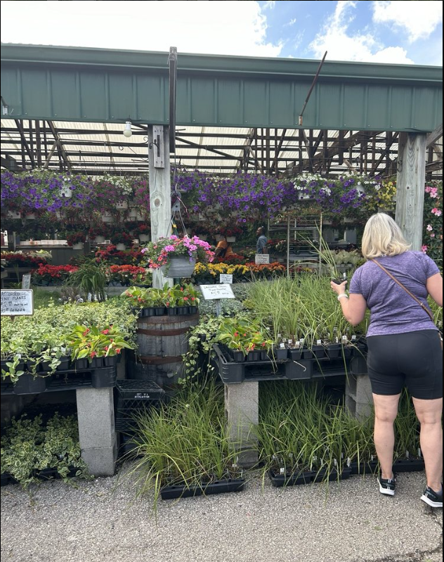 A woman is standing in front of a display of potted plants at a garden center.