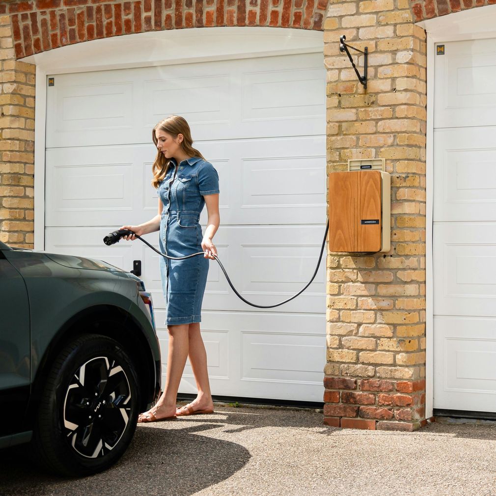 Woman charging an electric car in a driveway beside a garage.