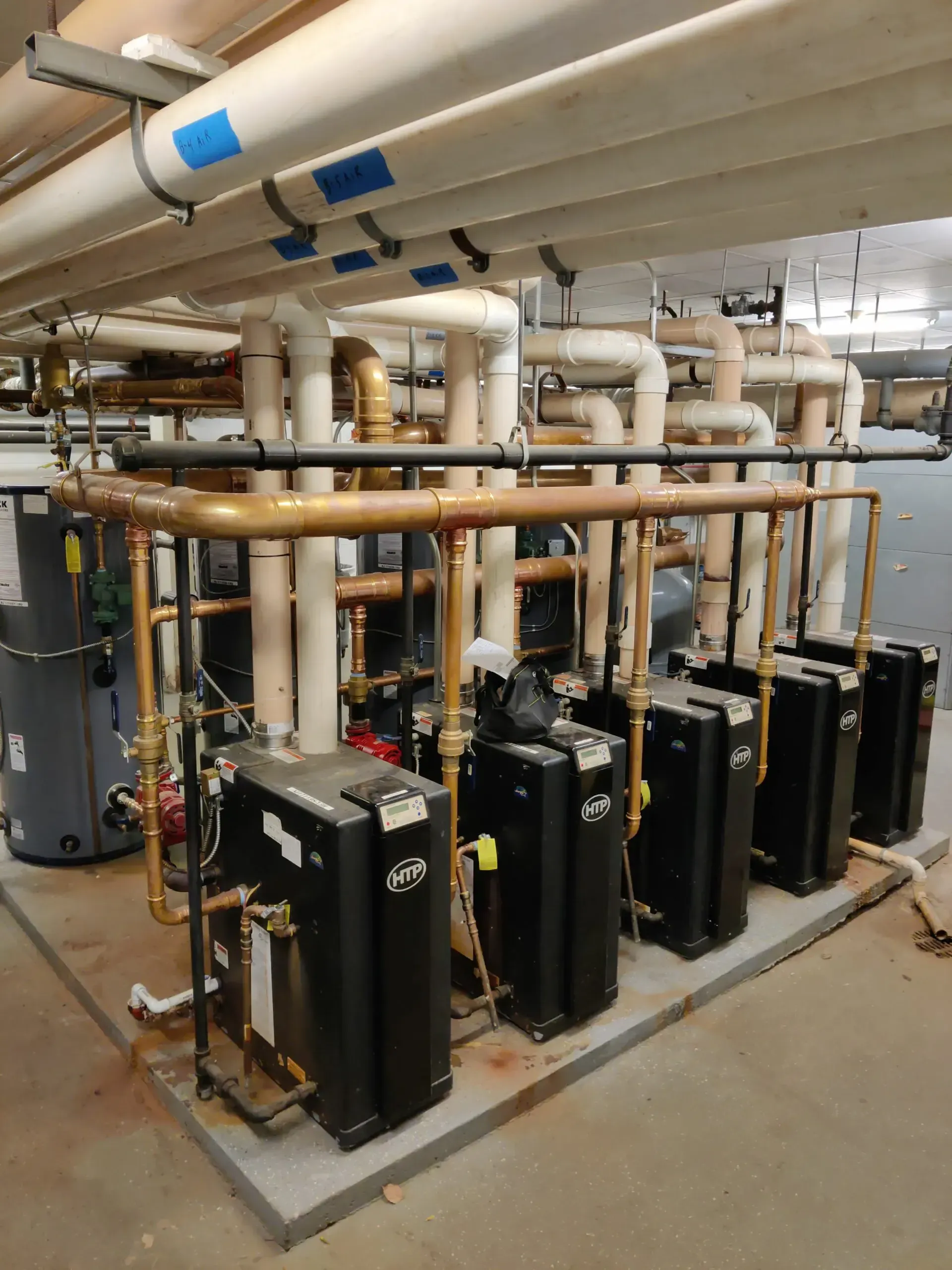 A row of boilers are lined up in a room with pipes