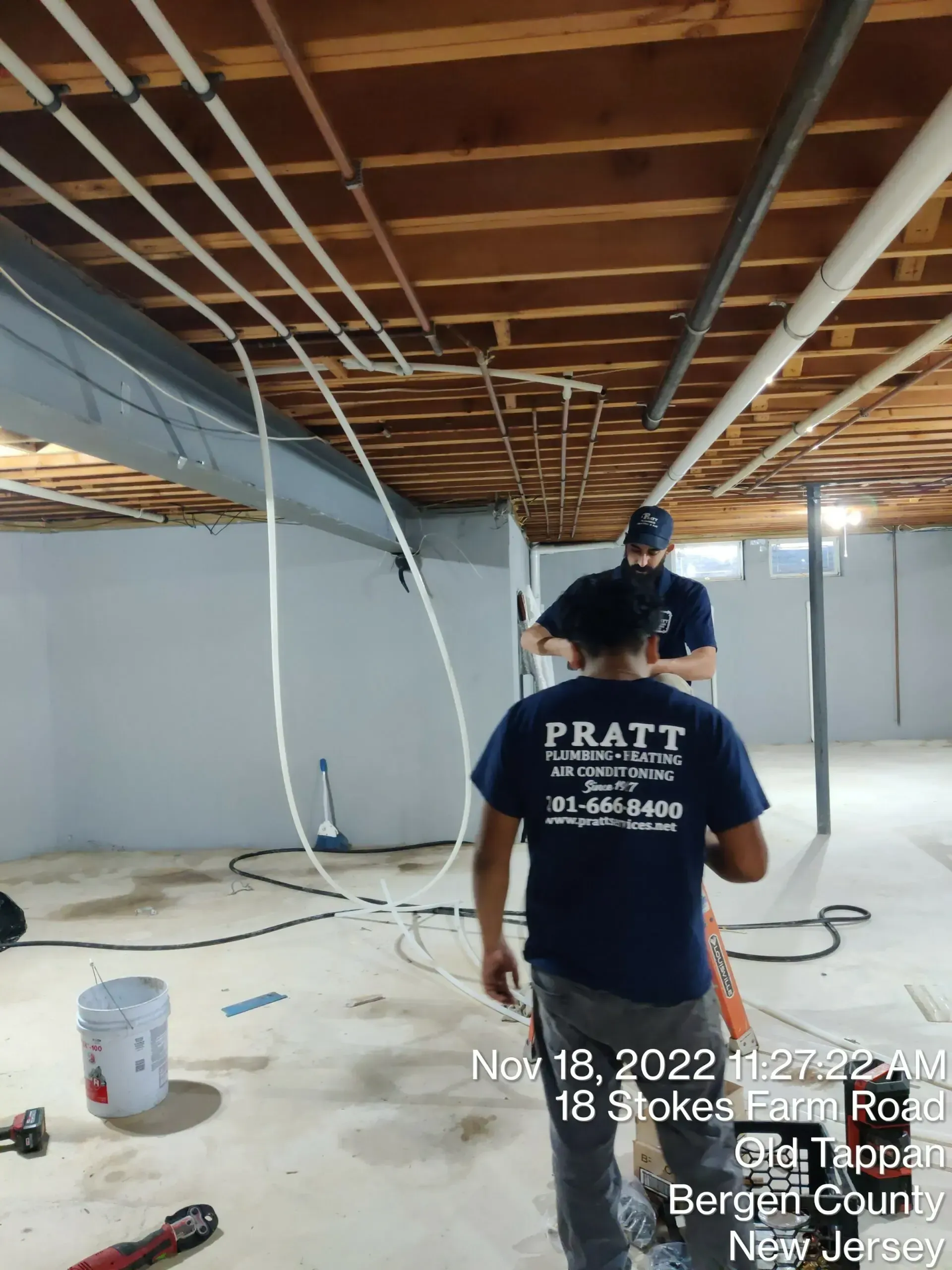 Two men are working on a basement ceiling.