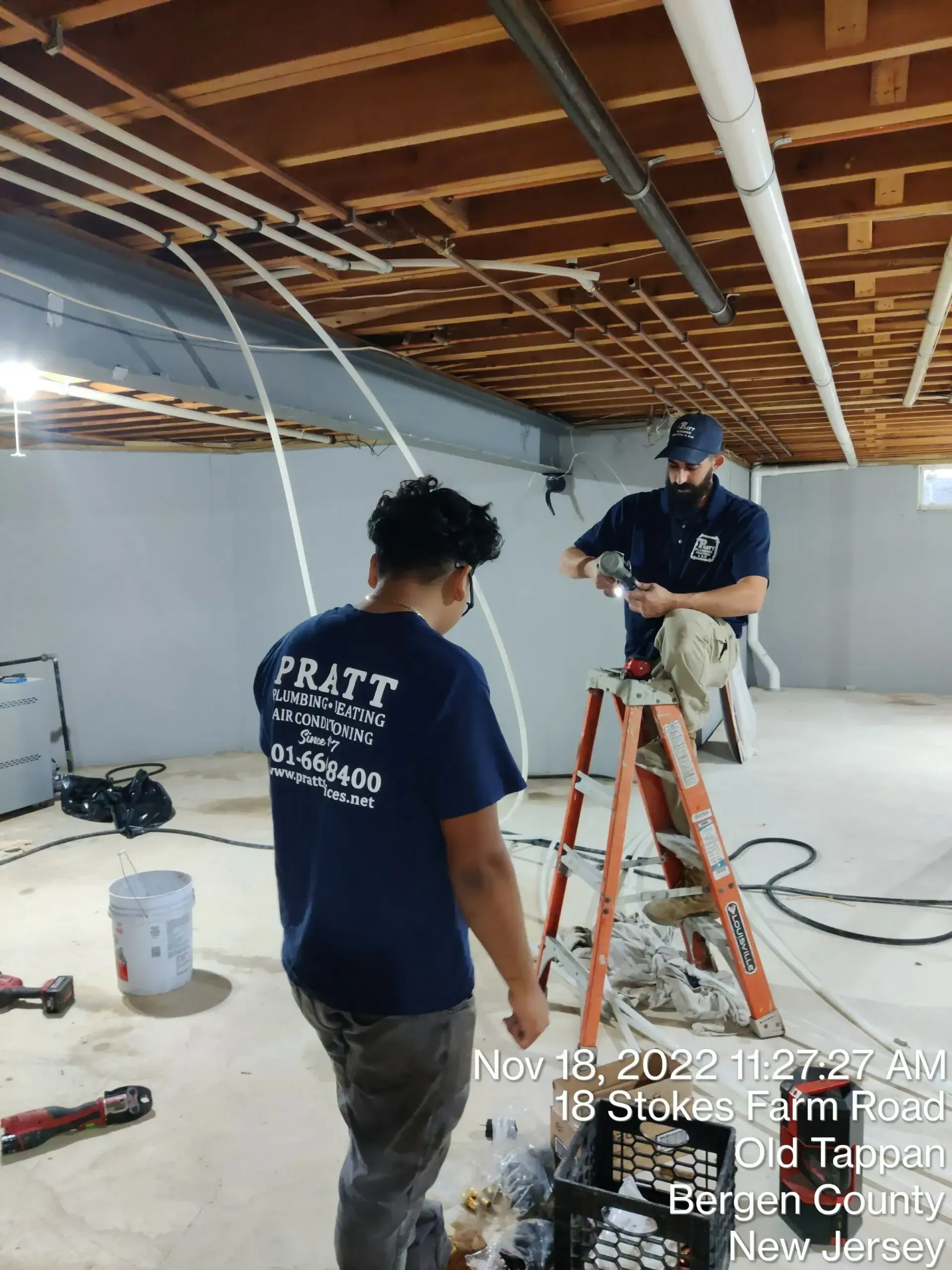 Two men are working on a ceiling in a basement.