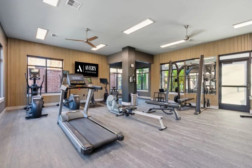 Gym with exercise equipment, including treadmills, weights, and rowing machines, with windows and light fixtures at The Avery at Orenco Station, offers apartments near Orenco Station Town Center.