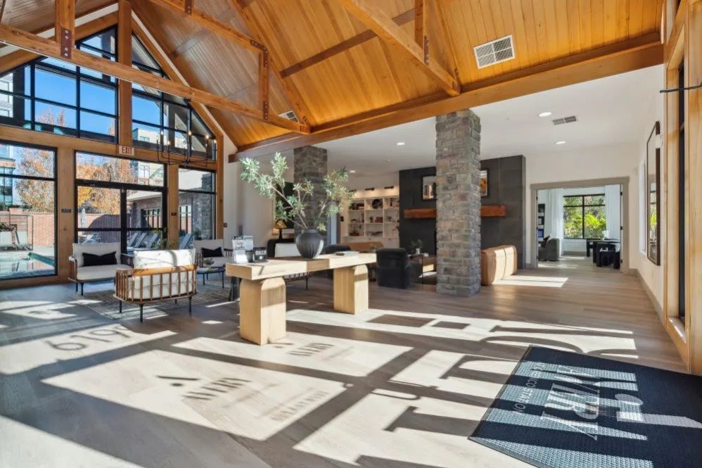 Lobby with wood beams and stone columns at The Avery at Orenco Station, offers apartments for rent in Hillsboro, OR. Sunlight streams across light wood floor.  Reception desk with plant decor.