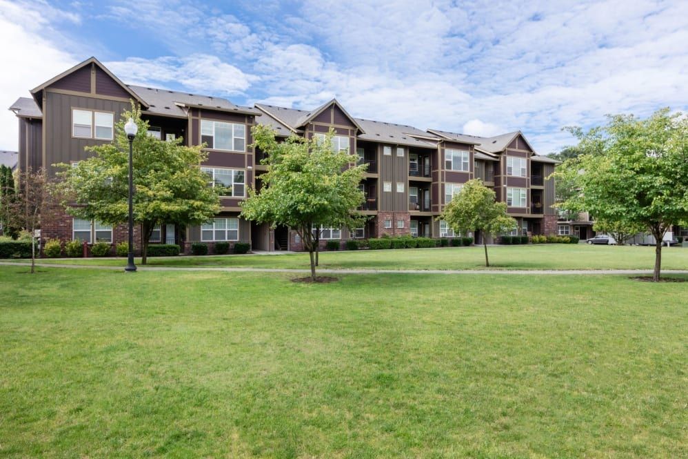 Brown apartment building with balconies, set on green lawn with trees, blue sky at The Avery at Orenco Station, offers apartments near Orenco Station Town Center.