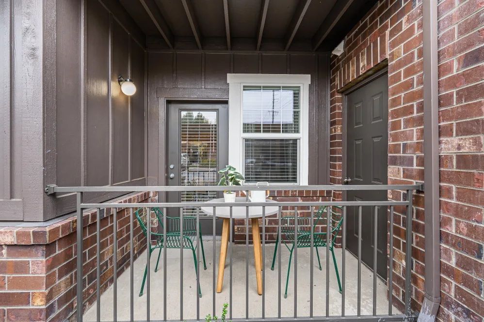Small balcony with green chairs, white table, brick, and brown siding at The Avery at Orenco Station, offers apartments for rent in Hillsboro, OR.