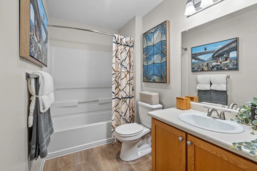 Bathroom with shower/tub, toilet, vanity, artwork, and towels at The Avery at Orenco Station, offers apartments in Hillsboro, OR. Light wood cabinets, grey walls.