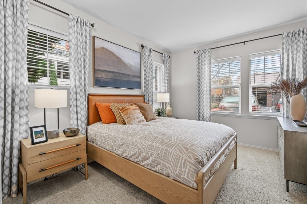 Bedroom with a bed, nightstands, and windows with patterned curtains. Artwork on the wall at The Avery at Orenco Station, offers apartments in Hillsboro, OR. 