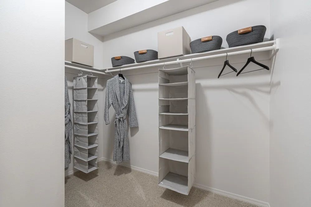 Walk-in closet with white shelves, hanging storage, and neutral-toned baskets, and a beige carpet at The Avery at Orenco Station, offers apartments in Hillsboro, OR. 
