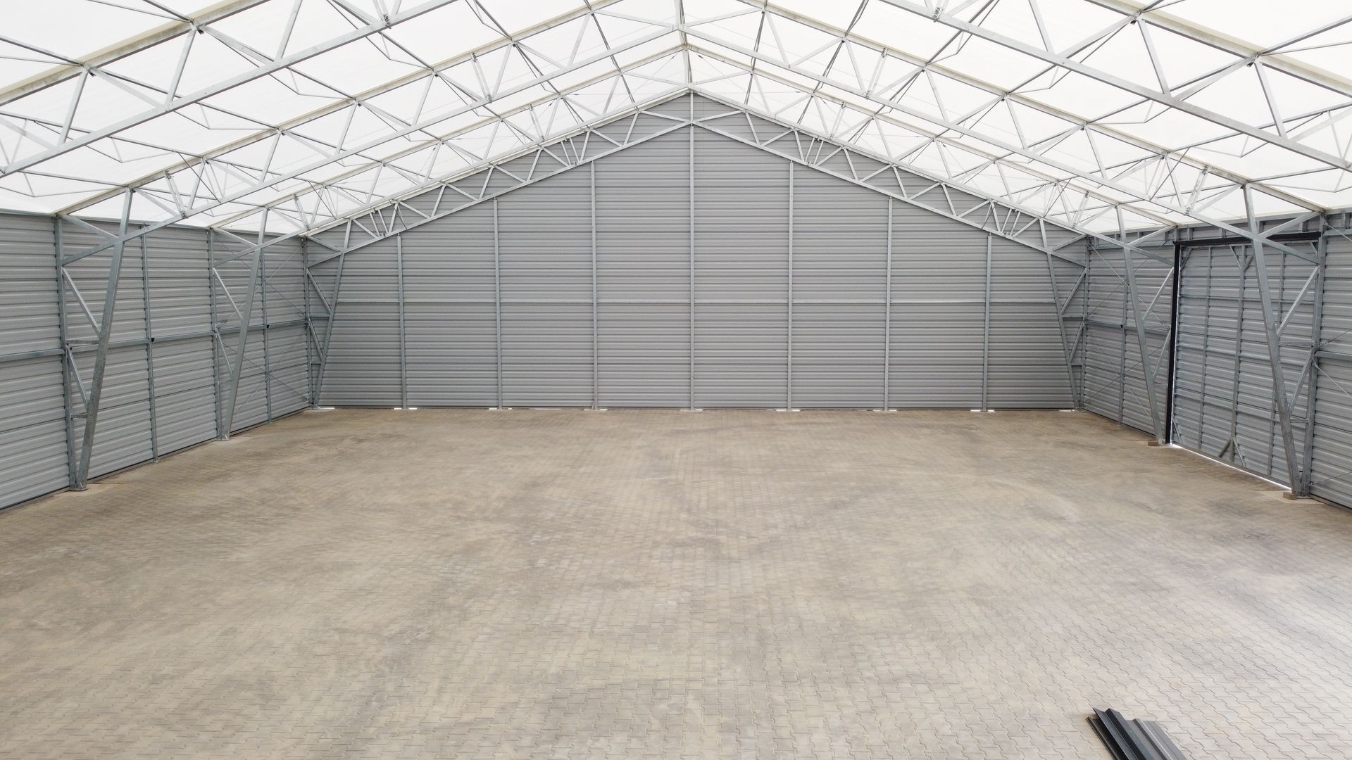 Puste wnętrze magazynu ze ścianami z szarej, falistej blachy i białym, namiotowym dachem spiczastym nad betonową podłogą.