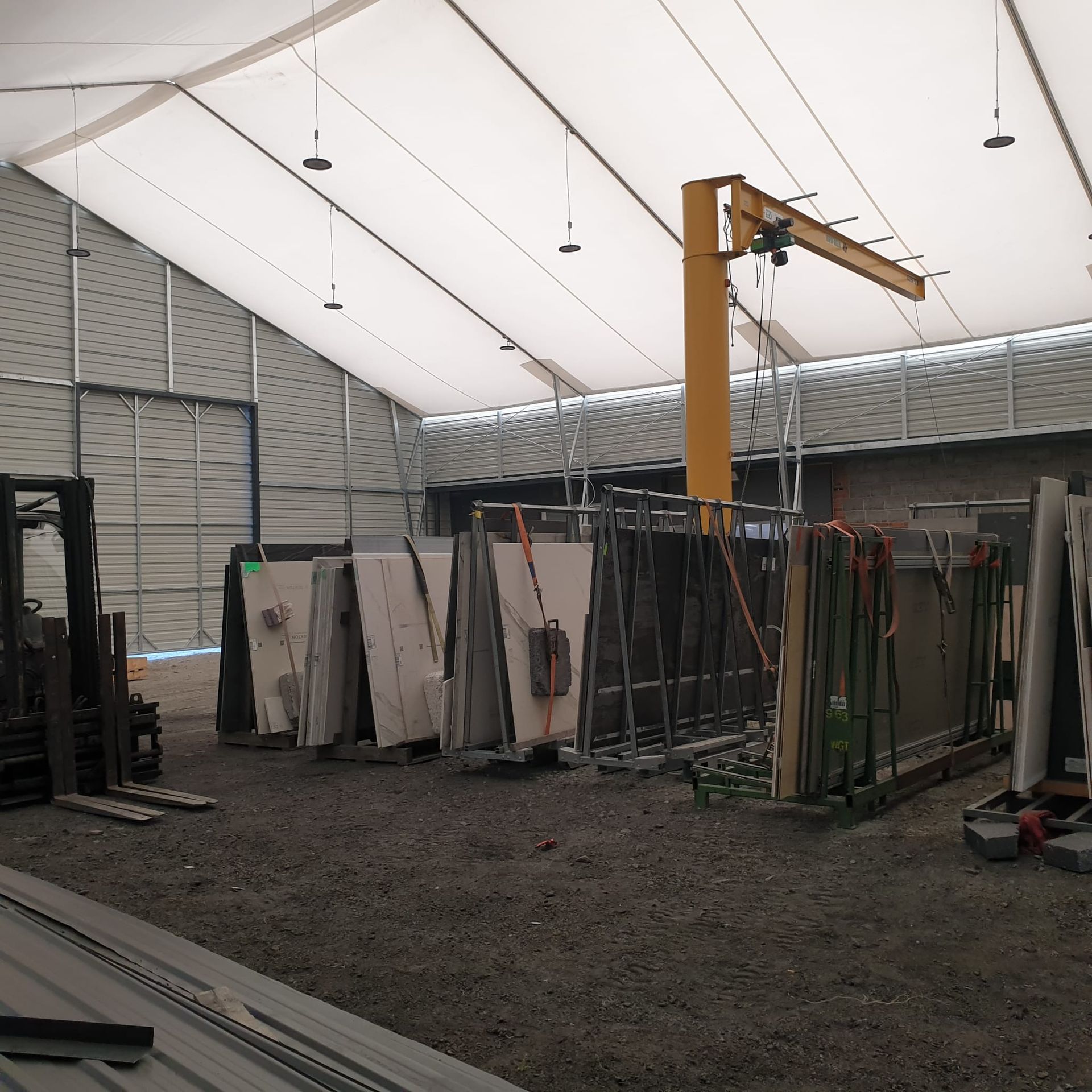 Duże płyty kamienne lub szklane składowane na pionowych regałach wewnątrz przestronnego, przemysłowego namiotu magazynowego.