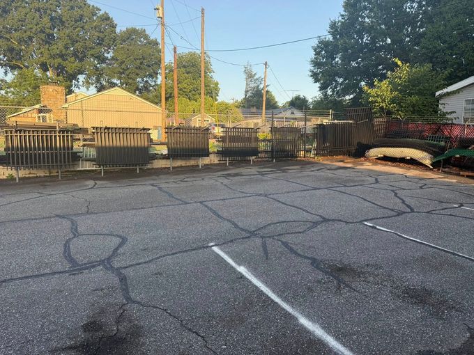 Paved parking lot with wooden structures in the background, trees, and power lines.