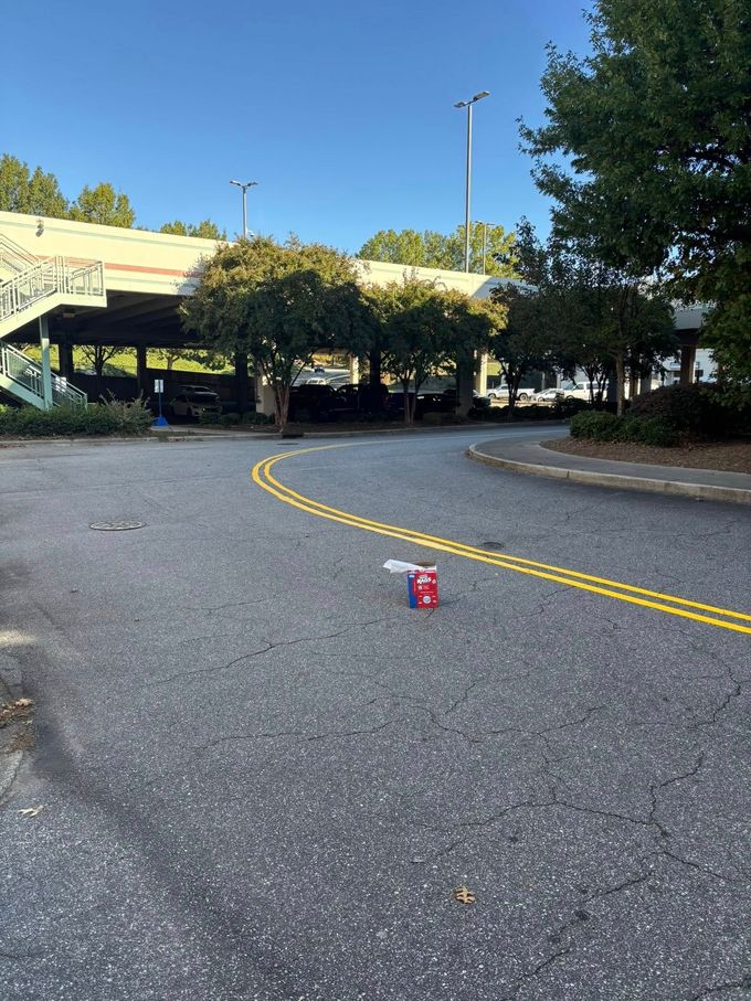 Asphalt road with double yellow lines, a discarded cigarette pack, and a covered parking area under a bridge.
