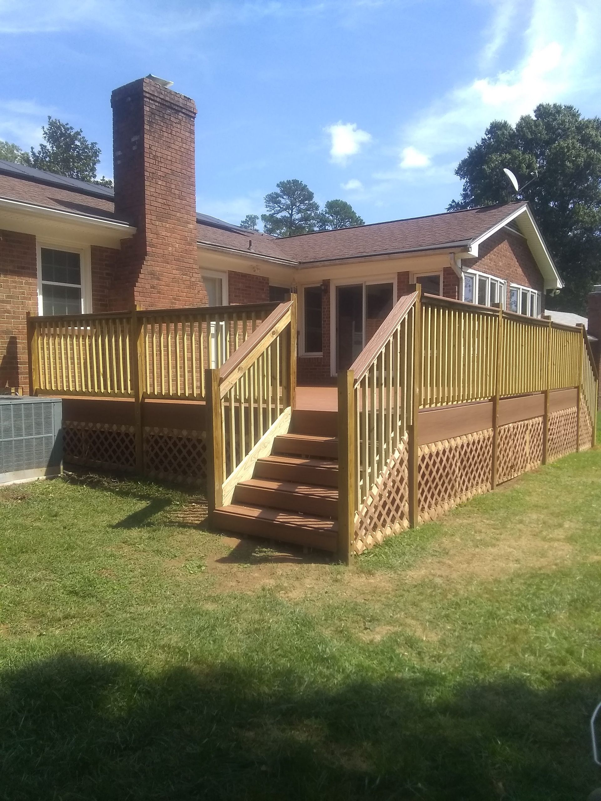 A gray deck with a white railing is in front of a green house.