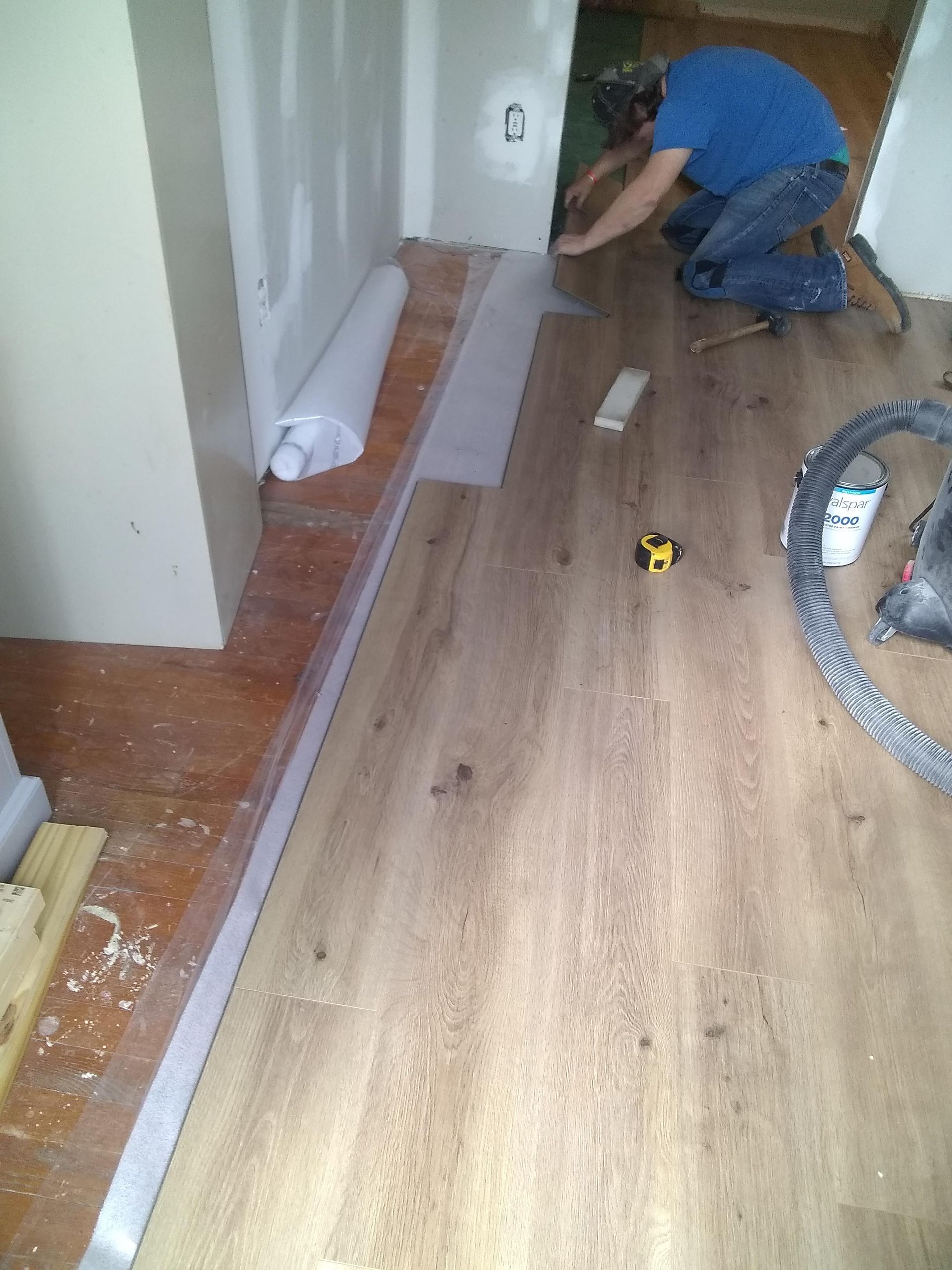 A man is kneeling down to install a wooden floor.