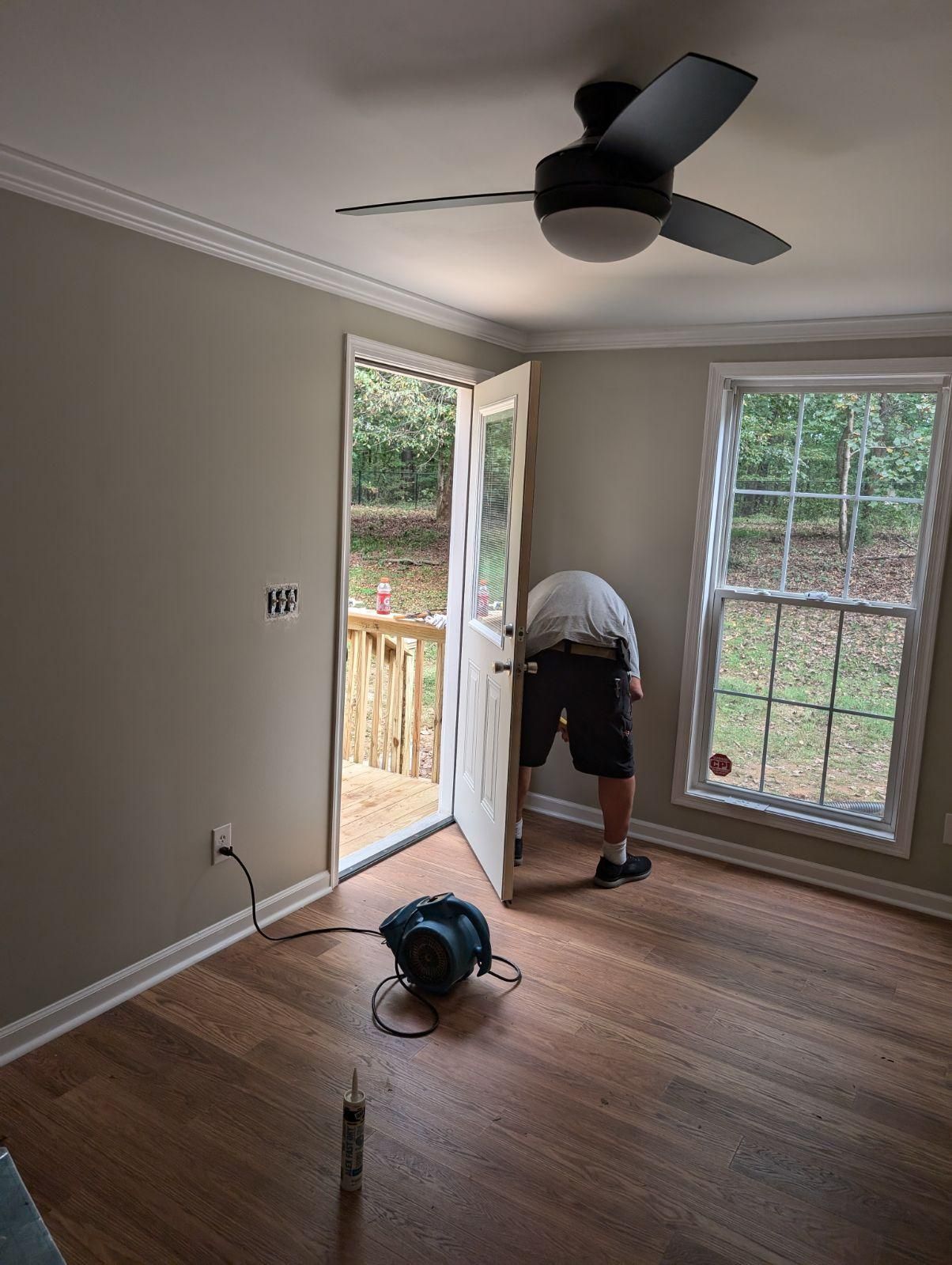 A man is installing hardwood flooring in a room with a ceiling fan.