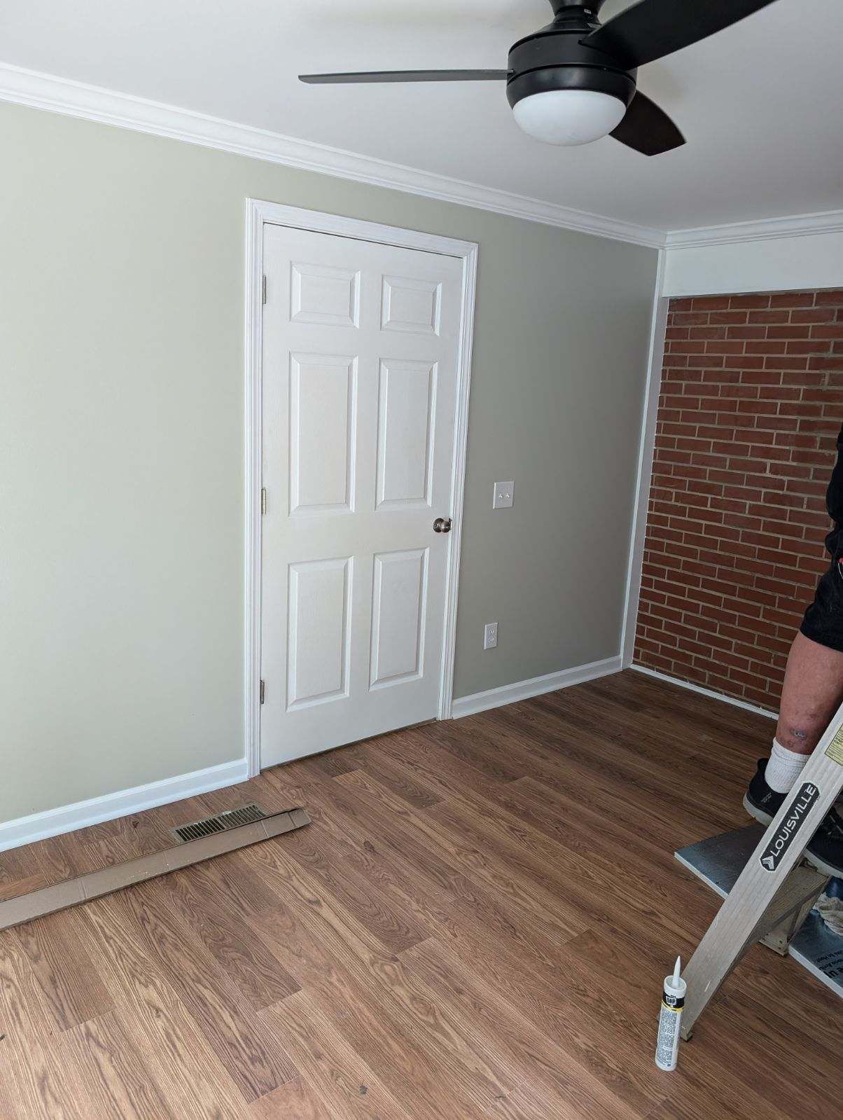 A person is standing in a room with a ceiling fan and a ladder.