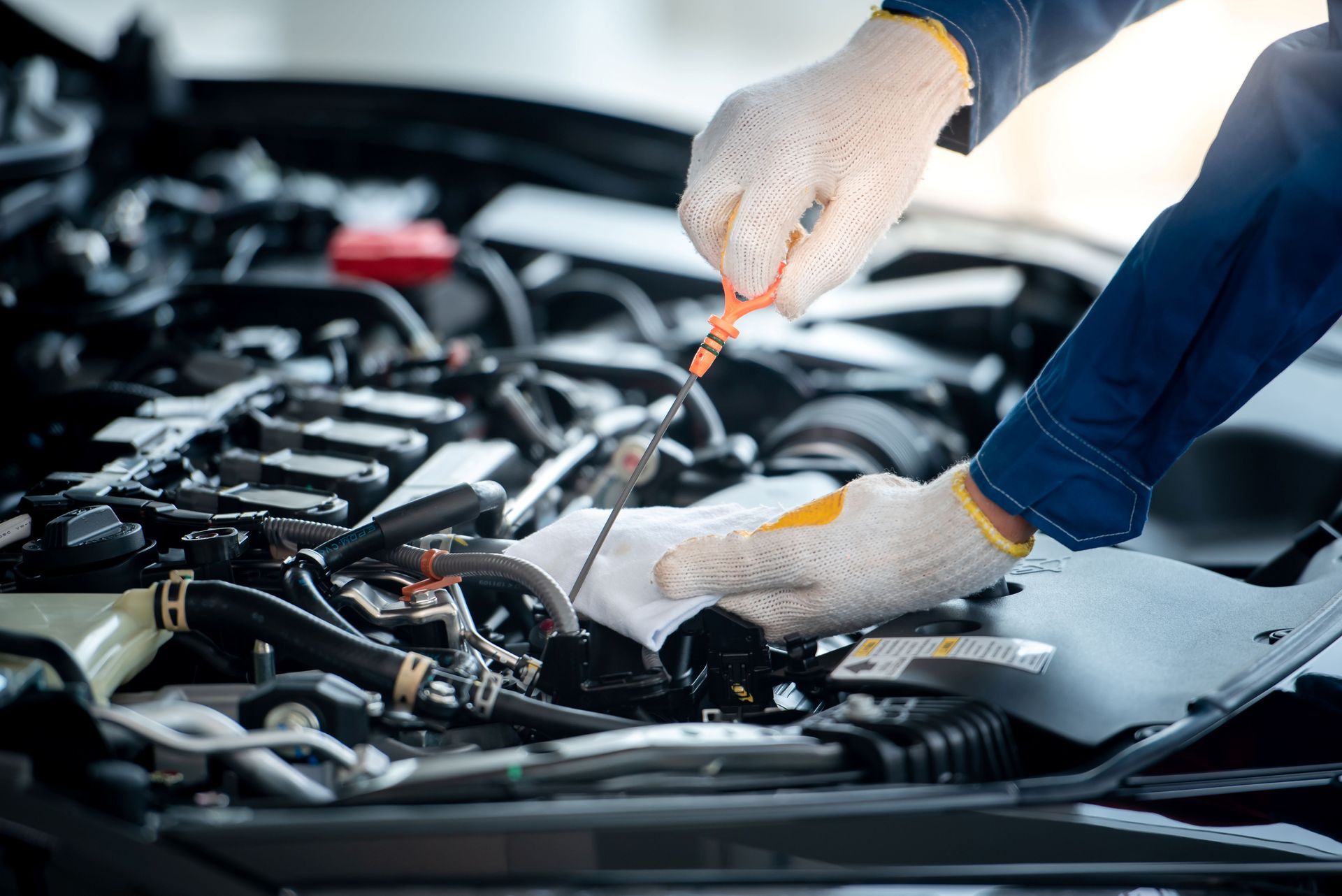 Mechanic checking engine oil with dipstick; wearing gloves.