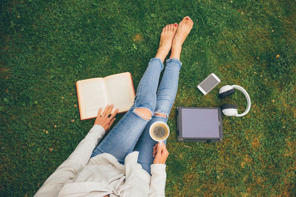 woman sitting in grass with drink and book