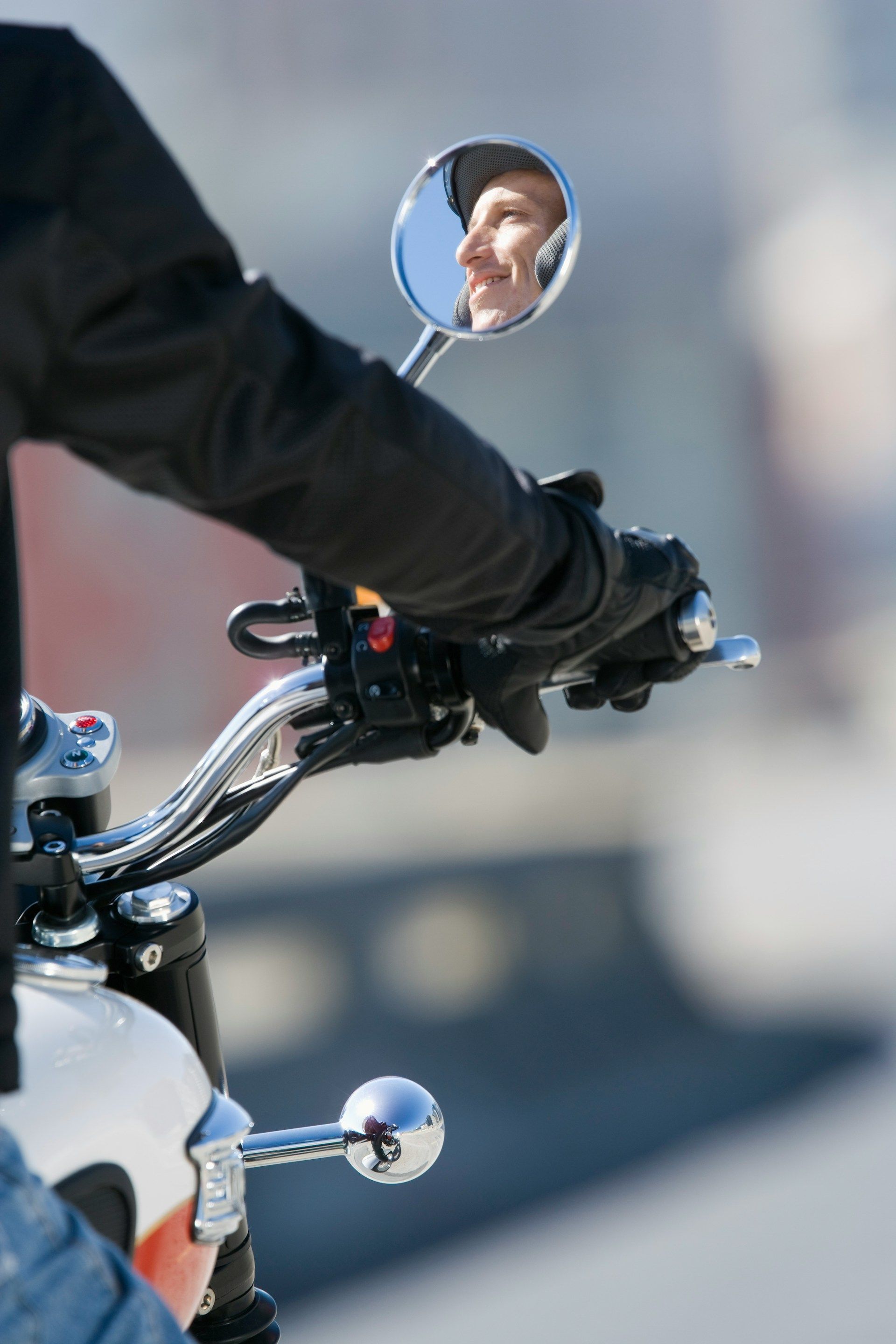Motorcyclist’s gloved hand on chrome handlebars, with a round mirror reflecting a face