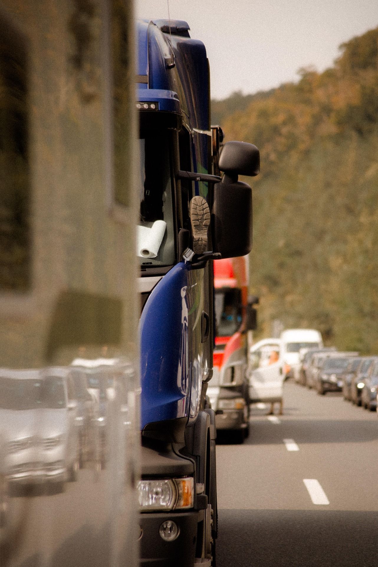 Truck convoy on a road, with a blue truck in the foreground and cars trailing behind.