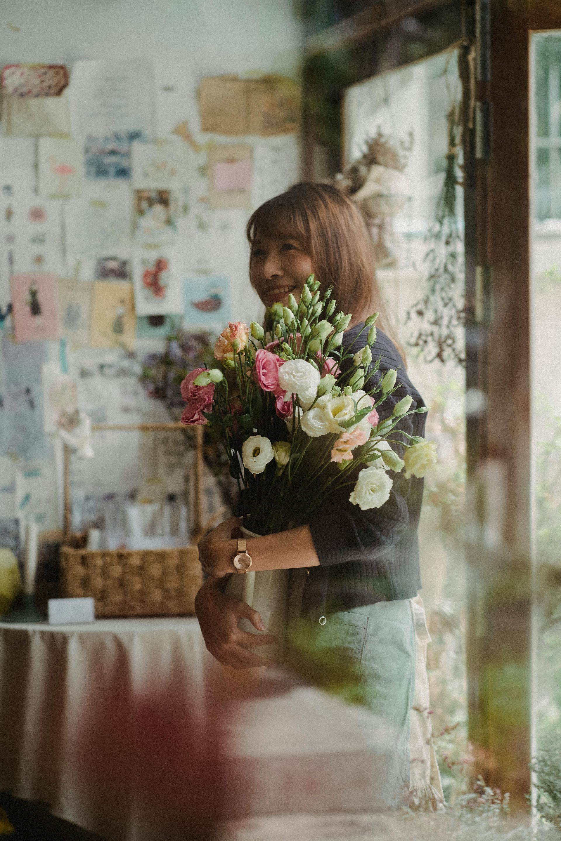 Smiling person holding a colorful bouquet in a softly lit room with floral decor