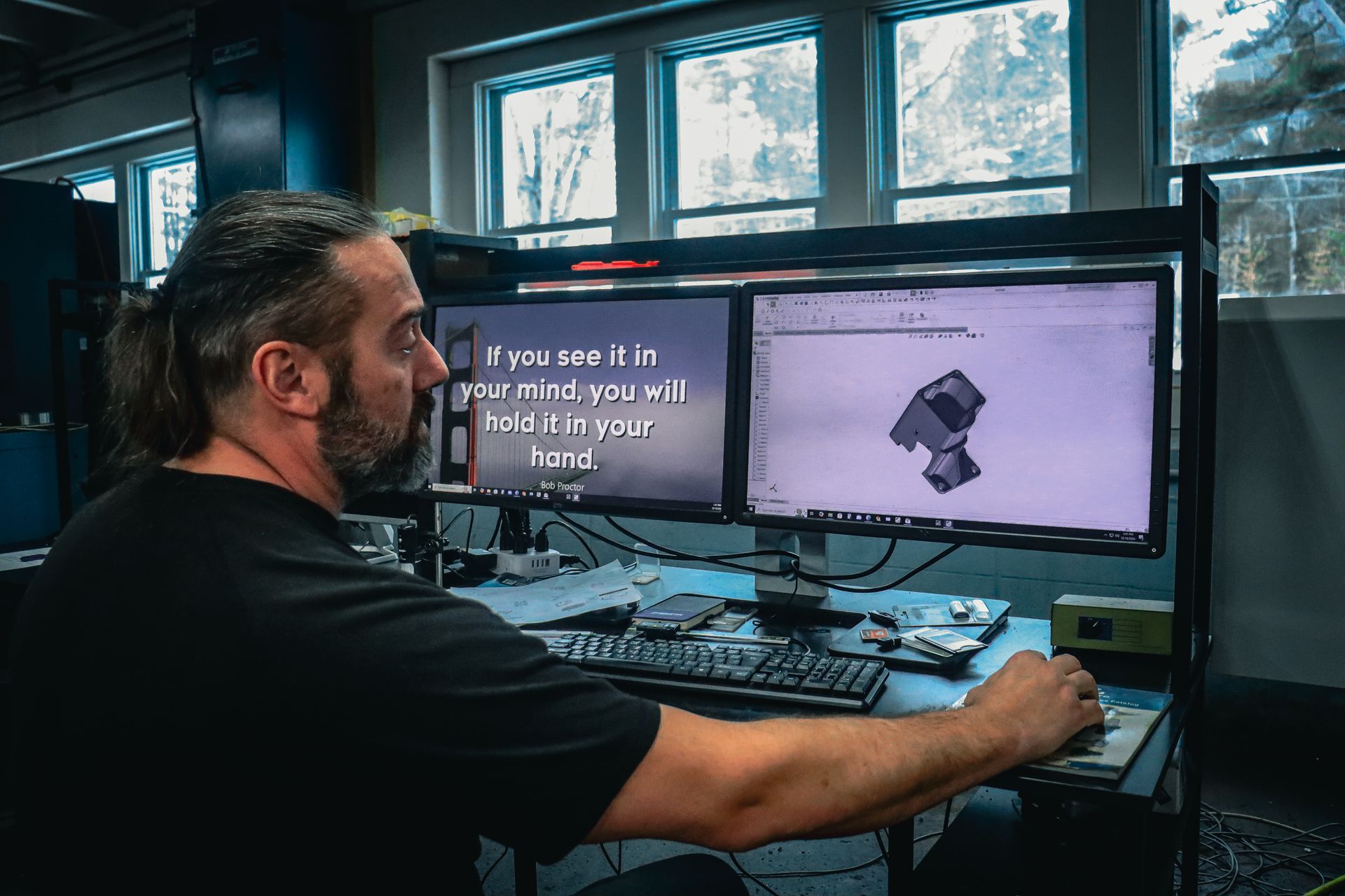 A man is sitting at a desk in front of two computer monitors.
