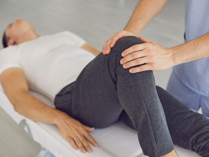 Physiotherapist examining a man's knee on a treatment table. The man lies still; the therapist manipulates the knee.