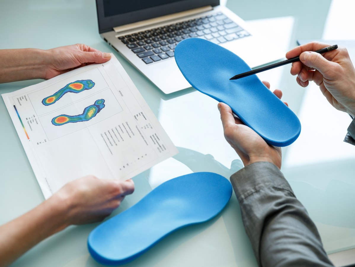 Two people examining foot pressure analysis results alongside blue orthotics.